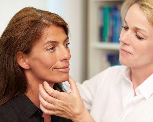 An elderly female patient with a suntanned complexion. Dermatologist at the private practice for dermatology examines her facial skin for blemishes. Frankfurt specialist creates an analysis of disturbing skin changes, which are removed.