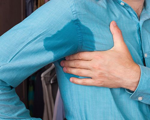 Man in a turquoise shirt. His armpits are wet from excessive sweating. The sweat soaked the shirt. He's holding his right armpit with his left hand because it's uncomfortable. There are treatments for excessive sweating.