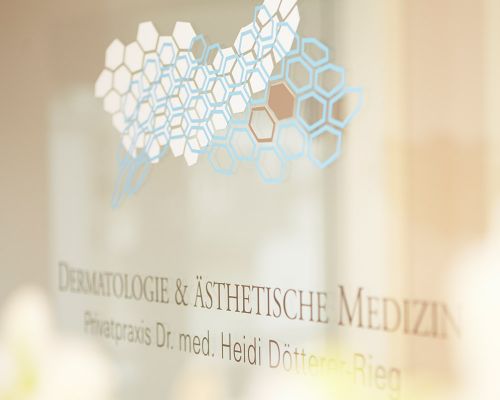 Orchids and corporate symbols on a glass door of the private practice for dermatology and aesthetic medicine in Frankfurt. White orchids are in the foreground. They are out of focus. In the background the practice symbol of the Frankfurt dermatologists.