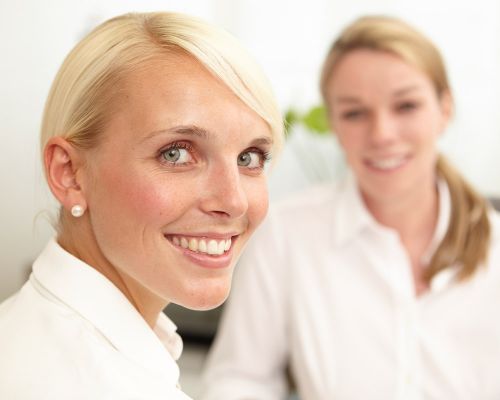 A woman at a consultation on treatment in dermatology, allergology, phlebology and podiatry. A satisfied patient in the dermatological private practice in Frankfurt/Main smiles at the camera. In the background sits the dermatologist Dr. Dötterer-Rieg.