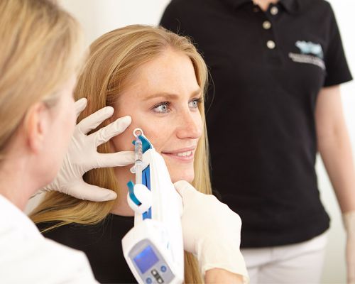 Young woman undergoing autologous blood treatment. The growth factors obtained from the patient's own blood are introduced into the skin of the face with the meso gun. The patient looks to the side with satisfaction while the doctor injects the PRP with micro-injections.
