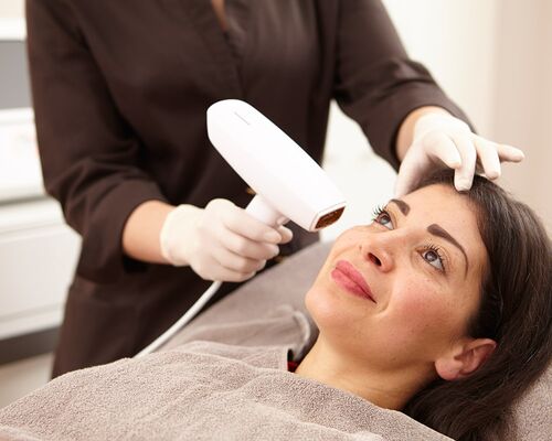 Gesicht einer Patientin wird mit der fraktionierten Radiofrequenz von Venus Viva™ behandelt. Die Kundin lächelt entspannt. Hände der Hautärztin in Handschuhe gekleidet, führen den RF-Behandlungskopf an den zu behandelnden Hautpartien des Gesichtes entlang