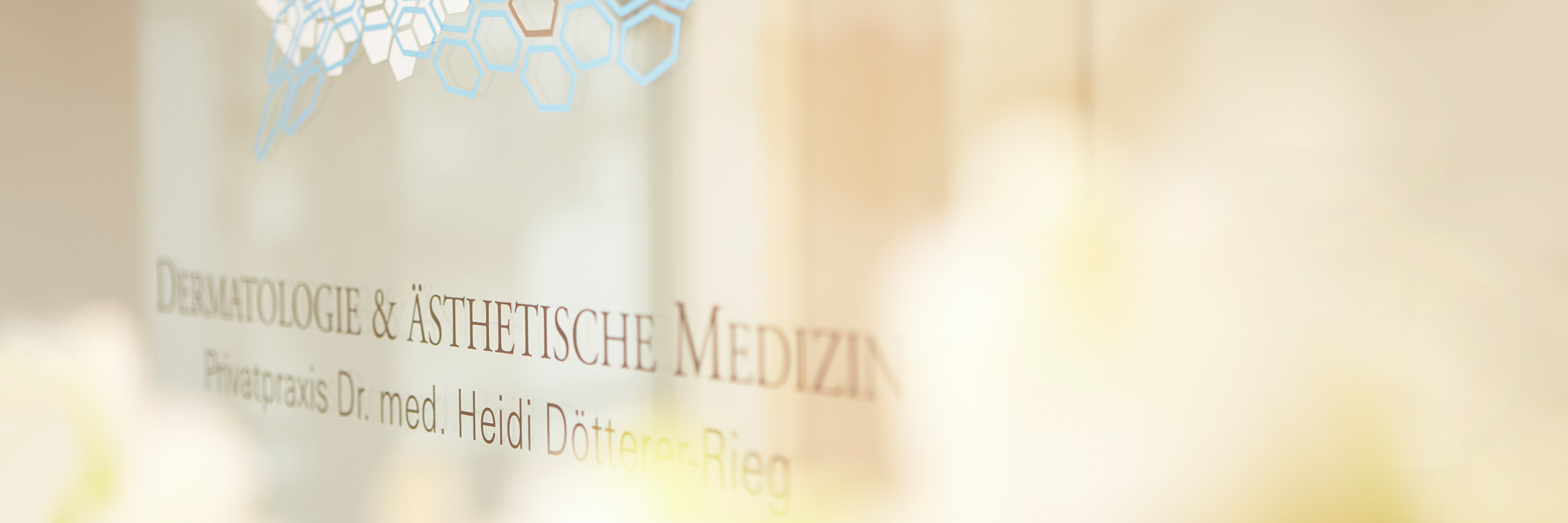 Privatpraxis Dr. med. Heidi Dötterer-Rieg & Kollegen für Dermatologie und Ästhetische Medizin ist auf einer Glastür angebracht. Im Vordergrund sind verschwommen frische weiße Orchideen zu sehen - Frankfurter Hautarztpraxis heißt Sie willkommen!