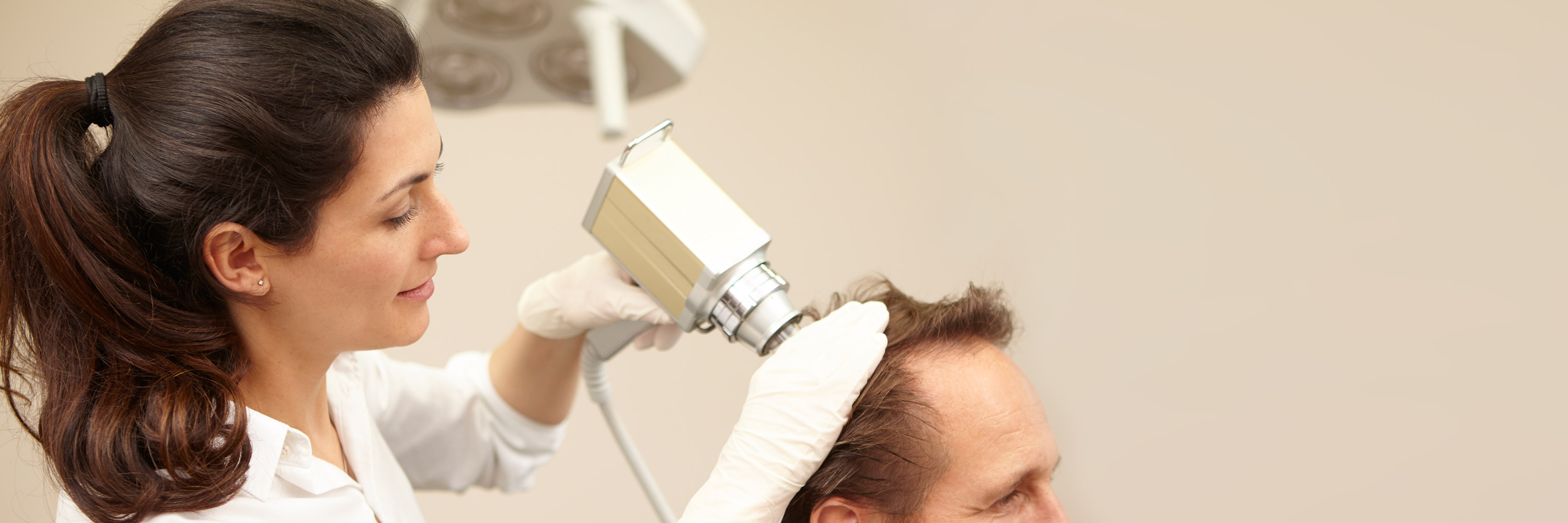 Fachärztin behandelt einen Patienten nach einer ausführlichen Sprechstunde mit der Mesopistole gegen Haarausfall. Die Haarwurzeln am Kopf einer männlichen Person werden durch die Injektionen mit der Mesopistole zum Wachstum angeregt.