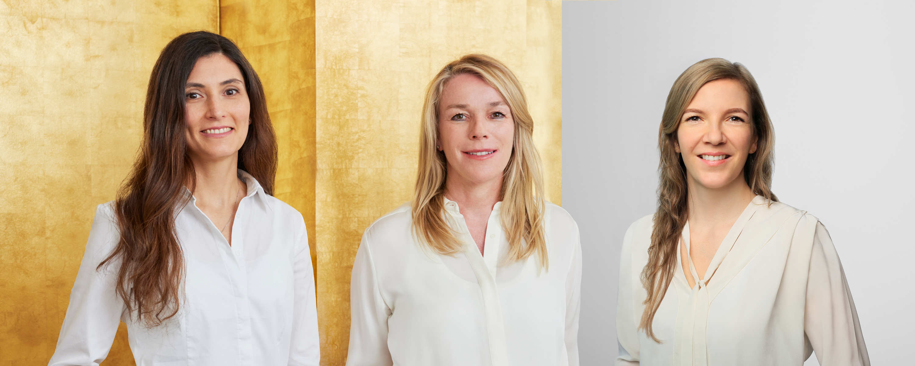Hautärzte unserer Hautarztpraxis in der Frankfurter Innenstadt stehen an einer Säule vor einer goldenen Wand. Spezialisten in der klassischen und operativen Dermatologie, Allergologie, Phlebologie und ästhetischen Dermatologie tragen weiße Blusen.