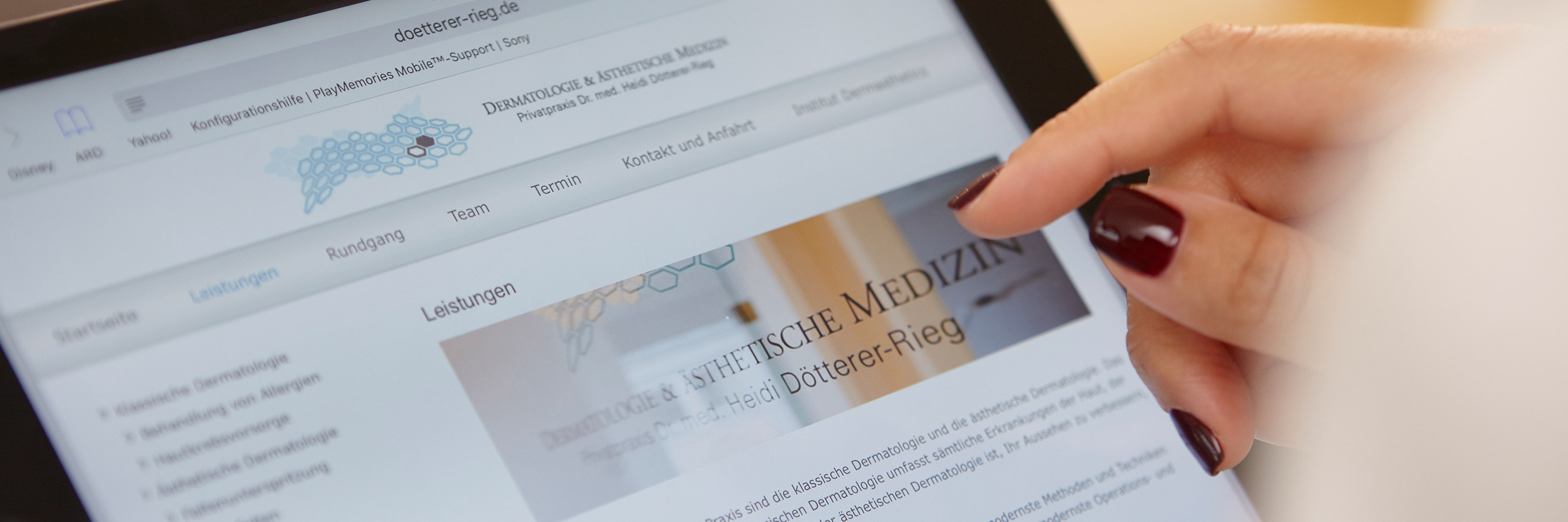 Ein Tablet wird von einer Patientin zur digitalen Terminvereinbarung bedient. Hände der Frau haben gepflegte Fingernägel und eine gesunde Haut. Dermatologische Patientin hat die Onlinepräsenz der Praxis für Dermatologie und ästhetische Medizin geöffnet.